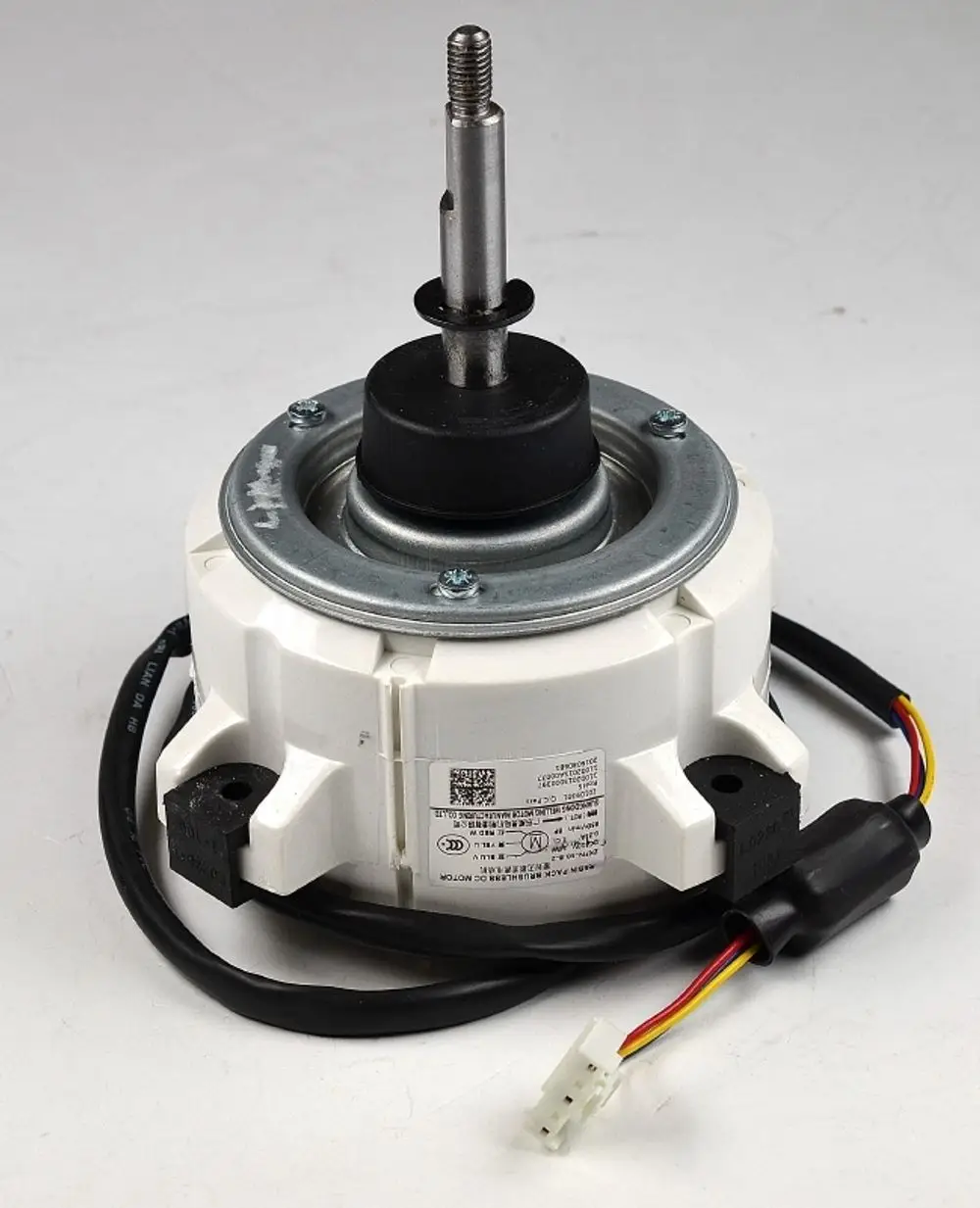 Remko Ventilatormotor mit einem zentralen Achsenstift und elektrischen Anschlüssen, montiert auf einer weißen Gehäusebasis. Kabel sind sichtbar und verlaufen seitlich.