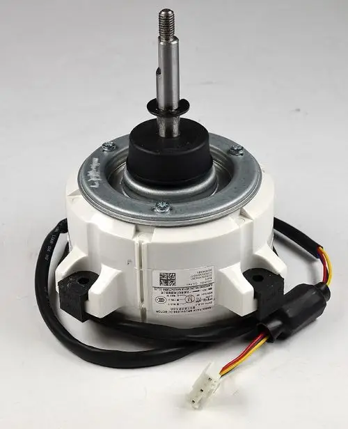 Remko Ventilatormotor mit einem zentralen Achsenstift und elektrischen Anschlüssen, montiert auf einer weißen Gehäusebasis. Kabel sind sichtbar und verlaufen seitlich.
