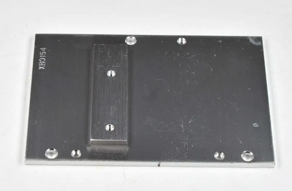 Aluminiumplatte mit mehreren Bohrungen und einer centralen Erhebung. Produkt von Remko, geeignet für Montageanwendungen. Oberfläche zeigt leichte Gebrauchsspuren.