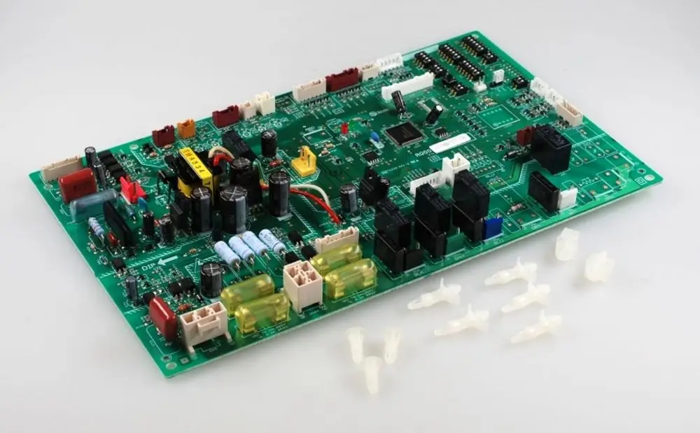 Grüne Steuerplatine mit verschiedenen elektrischen Komponenten und Anschlüssen, produziert von Remko. Im Vordergrund sind mehrere transparente Kunststoffteile sichtbar.