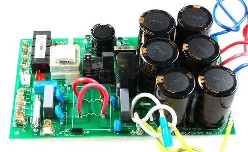 Leistungsplatine von Remko mit mehreren Kondensatoren, Relais, und Verbindungsdrähten auf einer grünen Leiterplatte. Elektronische Komponenten sind sichtbar angeordnet.