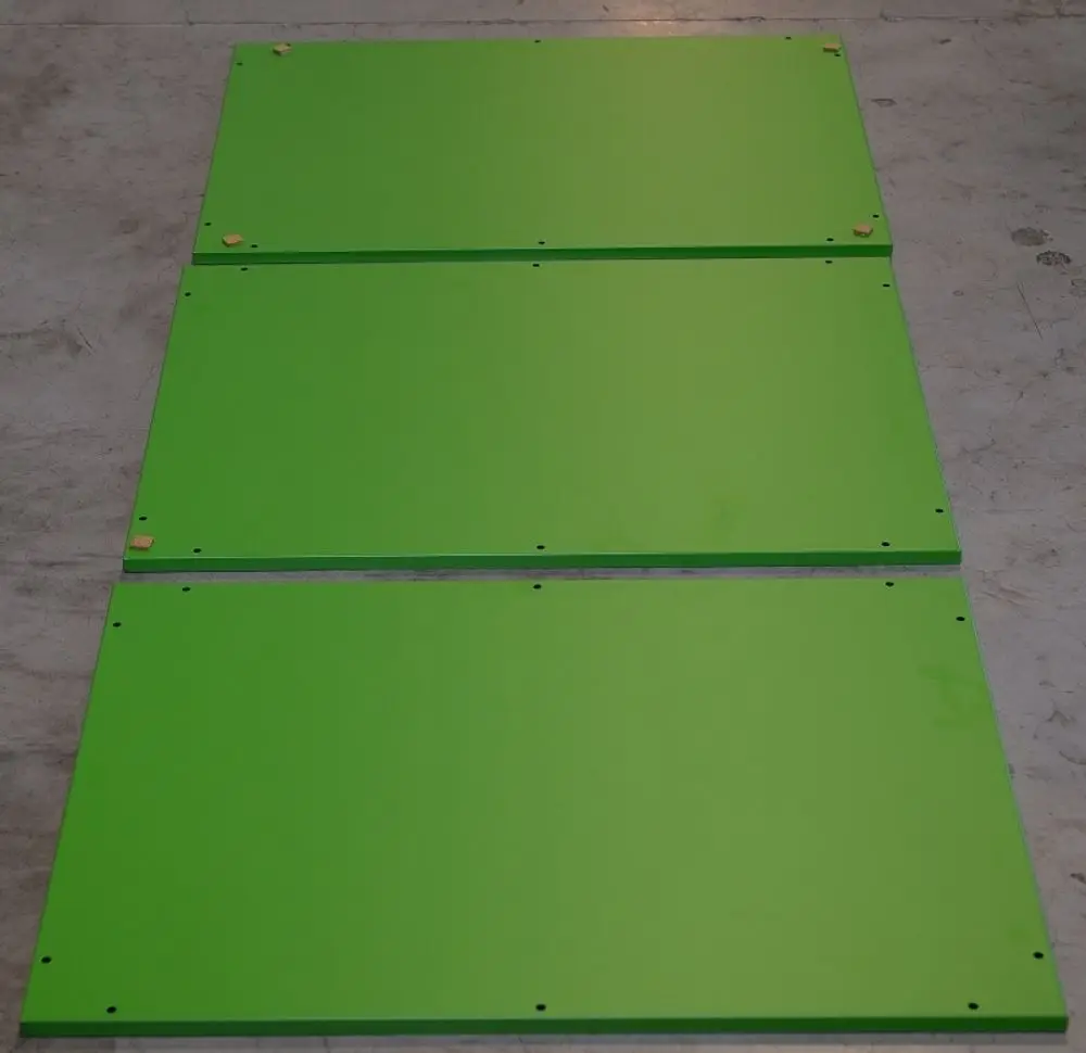 Drei grüne Metallplatten liegen nebeneinander auf einem grauen Untergrund. Sie sind mit Bohrlöchern versehen und könnten Teil eines Remko-Produkts sein.