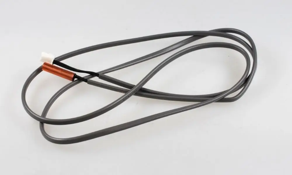 Sensor mit grauen Kabeln und einem weißen Stecker, auf dem ein kupferfarbener Abschnitt zu sehen ist. Produkt von Remko zur Flüssigkeitsleistungsmessung.