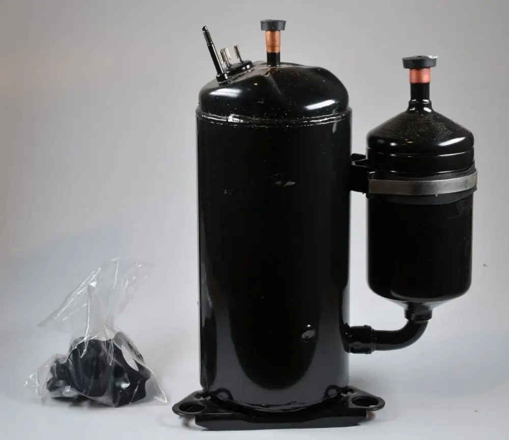 Remko-Kompressor in schwarzer Ausführung, mit zwei Anschlüssen oben, verbunden mit einem kleineren Behälter, daneben ein Plastikbeutel mit Zubehörteilen.