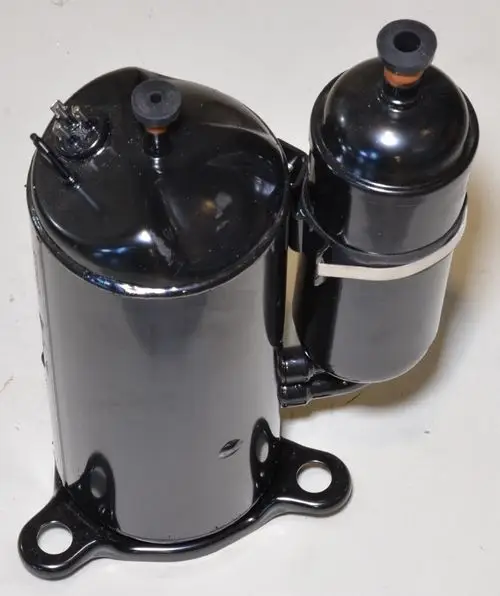 Schwarzer Kompressor mit zwei Elementen, einem größeren Hauptkörper und einem kleineren, seitlich angeordneten, von der Marke Remko. Installationsbasis mit Löchern zur Befestigung.