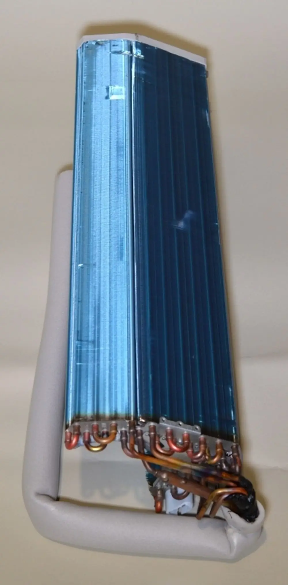 Remko-Verdampfer mit blauer Oberfläche und kupferfarbenen Rohren, montiert auf einer hellen Unterlage. Die Einheit zeigt eine kompakte Bauform.