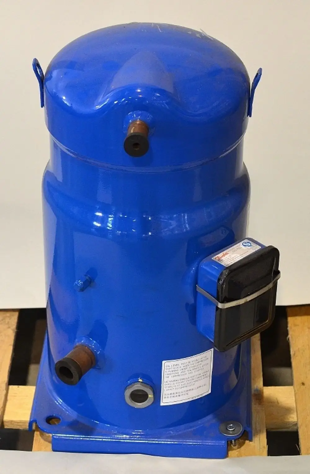 Blauer Kompressor von Remko, zylinderförmig mit zwei Anschlüssen an der Vorderseite und einem Anzeigegerät an der Seite, auf Holzpalette platziert.
