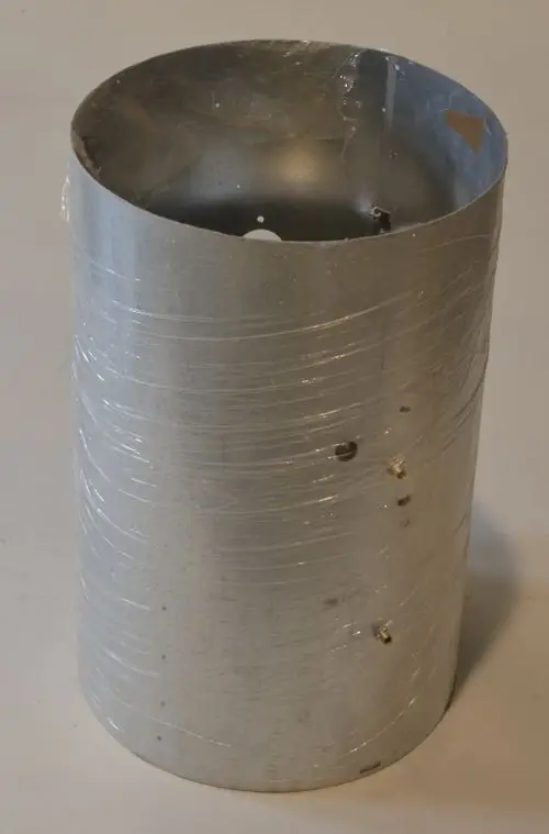 Einfache silberne Metallbrennkammer der Marke Remko, zylindrisch mit einer transparenten Folie umwickelt, an der Oberseite offen und mit mehreren Löchern an der Seitenfläche.