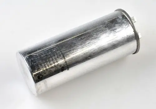 Silberner Kondensator in zylindrischer Form mit drei Anschlussklemmen. Beschriftung auf der Oberfläche vorhanden. Produkt von Remko.