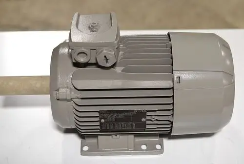 Remko Elektromotor in grauer Ausführung, mit aufrecht montierter Welle und seitlichem Anschluss. Technische Informationen auf der Typenschildfläche sichtbar.
