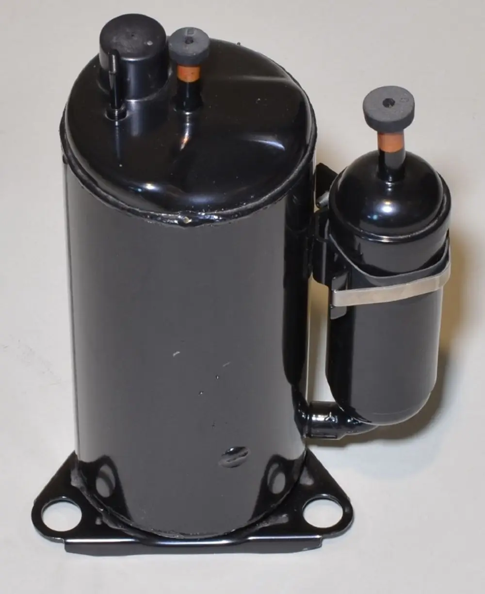 Schwarzer Kompressor mit runden Oberflächen und zwei Anschlüssen, befestigt an einer Halterung. Produkt von Remko, verwendet in Klimaanlagen oder Kühlgeräten.