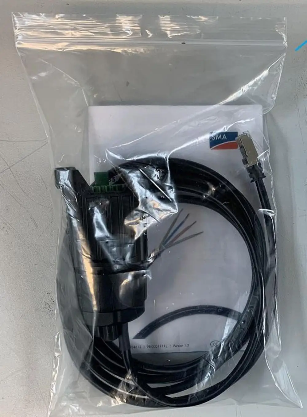 Ein Kommunikationskabel in einer Kunststoffverpackung, ausgestattet mit einem Stecker und mehreren Drähten, mit dem Markenlogo "SMA" auf einem beiliegenden Dokument.