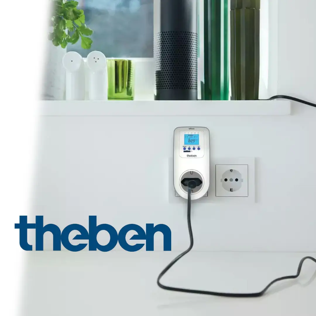 Digitale Steckdosen-Zeitschaltuhr von Theben, montiert in einer Steckdose, mit einem Display für Programmierung und Steuerung, umgeben von weiteren Haushaltsgeräten.