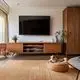 Holzregal mit Fernseher an der Wand, davor ein beigefarbener Teppich. Auf einem runden Hundebett liegt ein Hund. Links ein Pflanzengefäß und eine gemütliche Sitzecke. Theben Produkte sind nicht sichtbar.