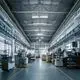 Blick in eine helle Fabrikhalle mit Maschinen auf beiden Seiten. Die Werkbank ist mit verschiedenen Geräten ausgestattet, die eine industrielle Umgebung schaffen.