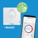 Theben Digitalthermostat mit Bluetooth-Funktion, angezeigt auf einem blauen Hintergrund. Smartphone zeigt Temperaturdaten und Steuerung des Thermostats.