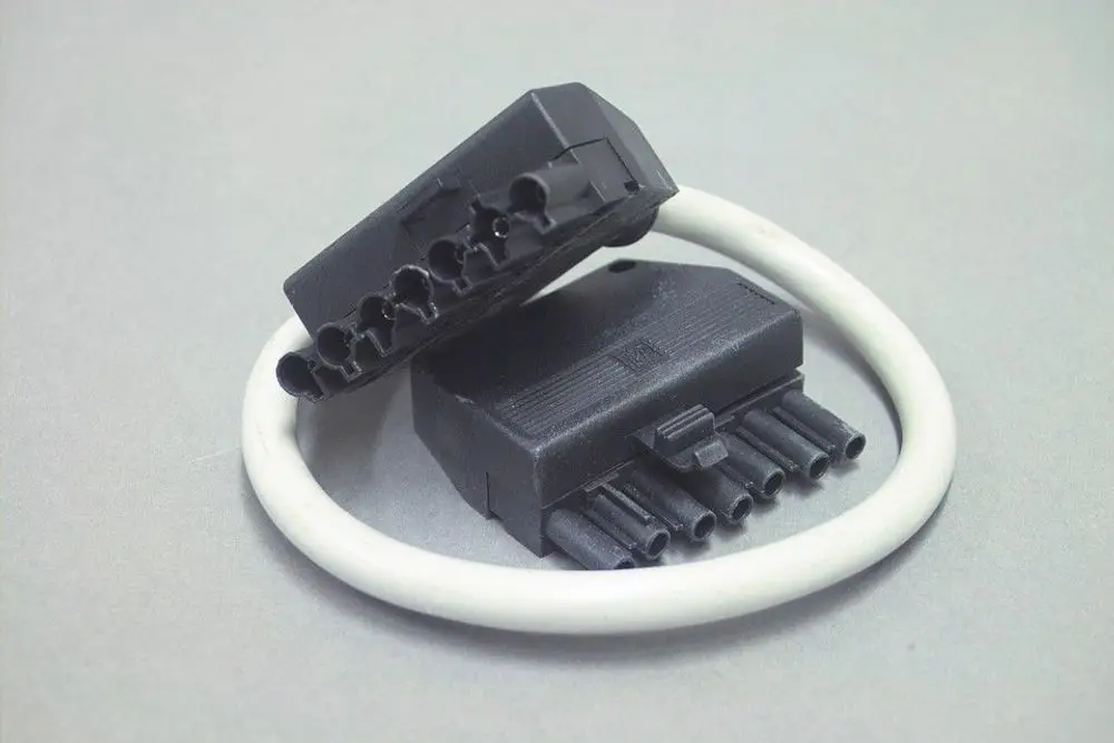 Stecker aus Kunststoff mit mehreren Anschlussbuchsen, möglicherweise von Brötje, auf grauem Untergrund. Ein Kabelring umschließt die Stecker.