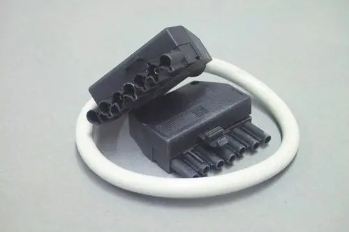 Stecker aus Kunststoff mit mehreren Anschlussbuchsen, möglicherweise von Brötje, auf grauem Untergrund. Ein Kabelring umschließt die Stecker.