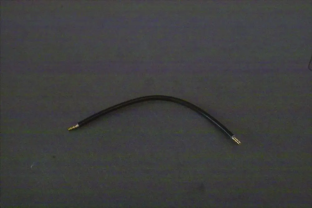 Schwarzes Kabel mit zwei goldenen Steckern an den Enden, auf einer dunklen Unterlage. Produkt von Brötje.