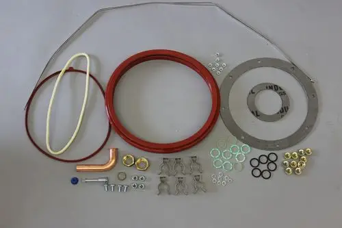 Verschiedene Metall- und Kunststoffkomponenten sowie Dichtungen und Ringe, wahrscheinlich für einen Wärmetauscher von Brötje, angeordnet auf einem neutralen Hintergrund.