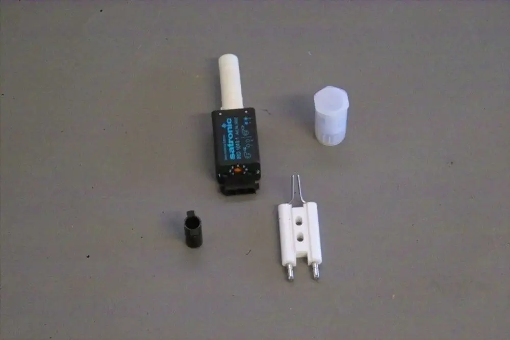 Ein Set bestehend aus mehreren Komponenten, darunter ein schwarzes Bauteil mit Anschluss, ein weißer Stift und ein kleiner schwarzer Zylinder, hergestellt von Brötje.