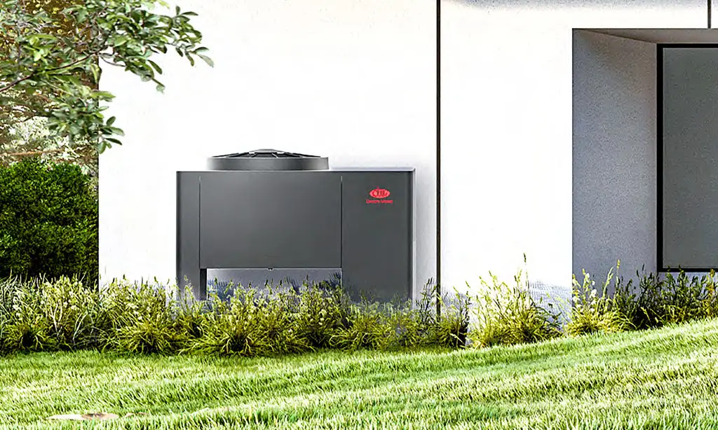 Schwarzes Außenteil einer Wärmepumpe von Dream Maker, auf einem Rasen vor einer weißen Wand, umgeben von grünen Sträuchern und Gras.