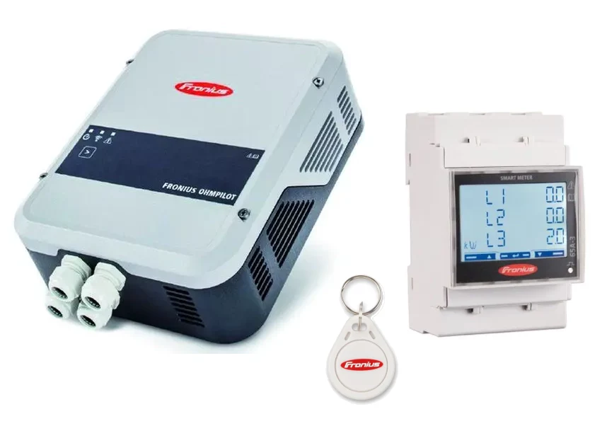 Fronius Ohmpilot Lieferumfang — Steuergerät in Hellgrau mit Kabelverschraubungen, Fronius Smart Meter mit LCD-Display auf Hutschiene und RFID-Schlüsselanhänger