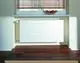 Ein weißer Heizkörper vor einer Wand mit einem Fenster mit Jalousien und einer Schale mit Äpfeln.