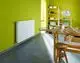 Ein weißer Heizkörper hängt an einer grünen Wand in einem Raum mit grauem Fliesenboden.