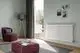Ein Wohnraum mit einem weißen Kermi Pio Heizkörper an der Wand, einem Sessel und einem grauen Teppich.